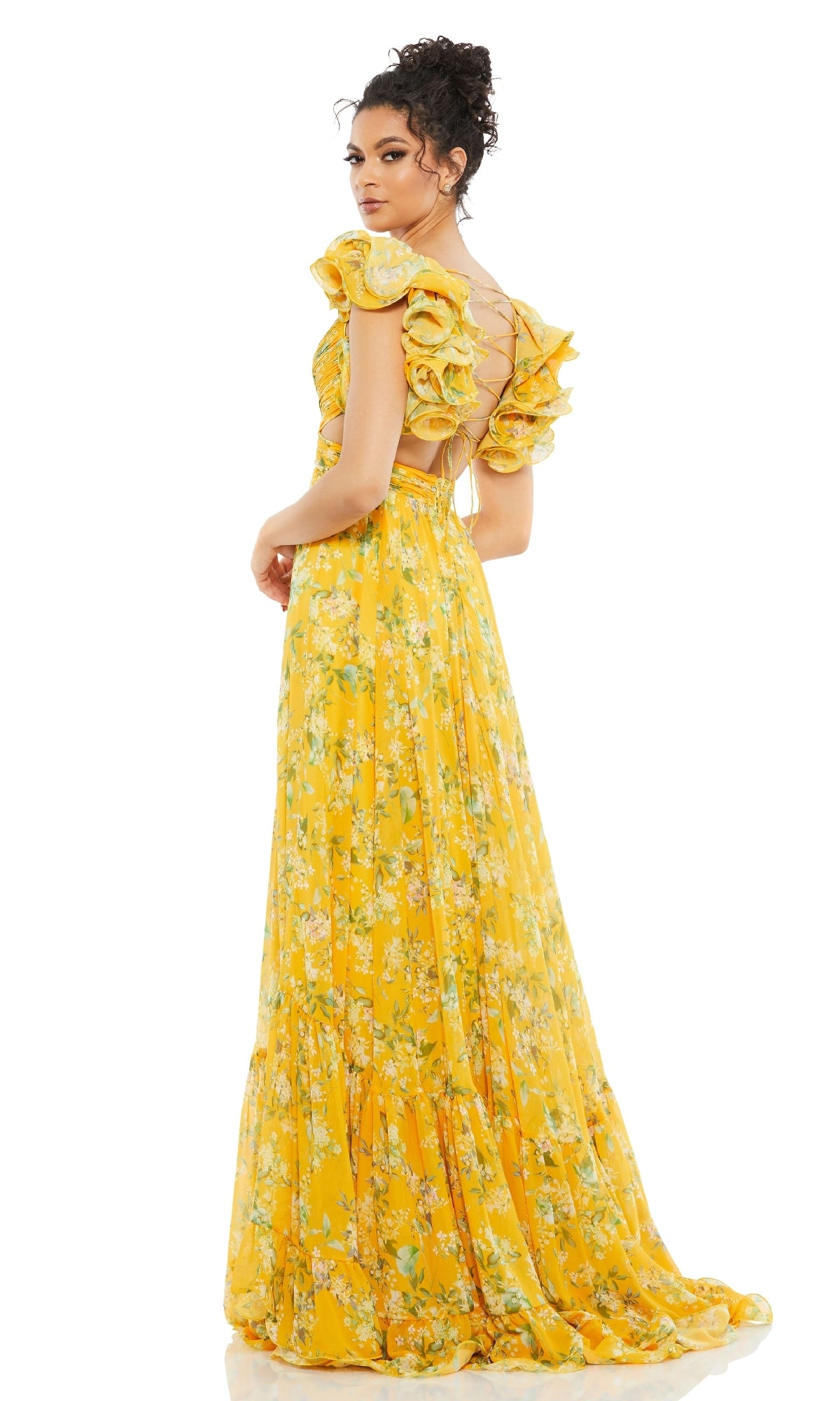 A woman models the Mac Duggal 67803 Ruffled Long Print Formal Dress, featuring a yellow floral print, ruffled short sleeves, and an open back as she looks over her shoulder against a white background.